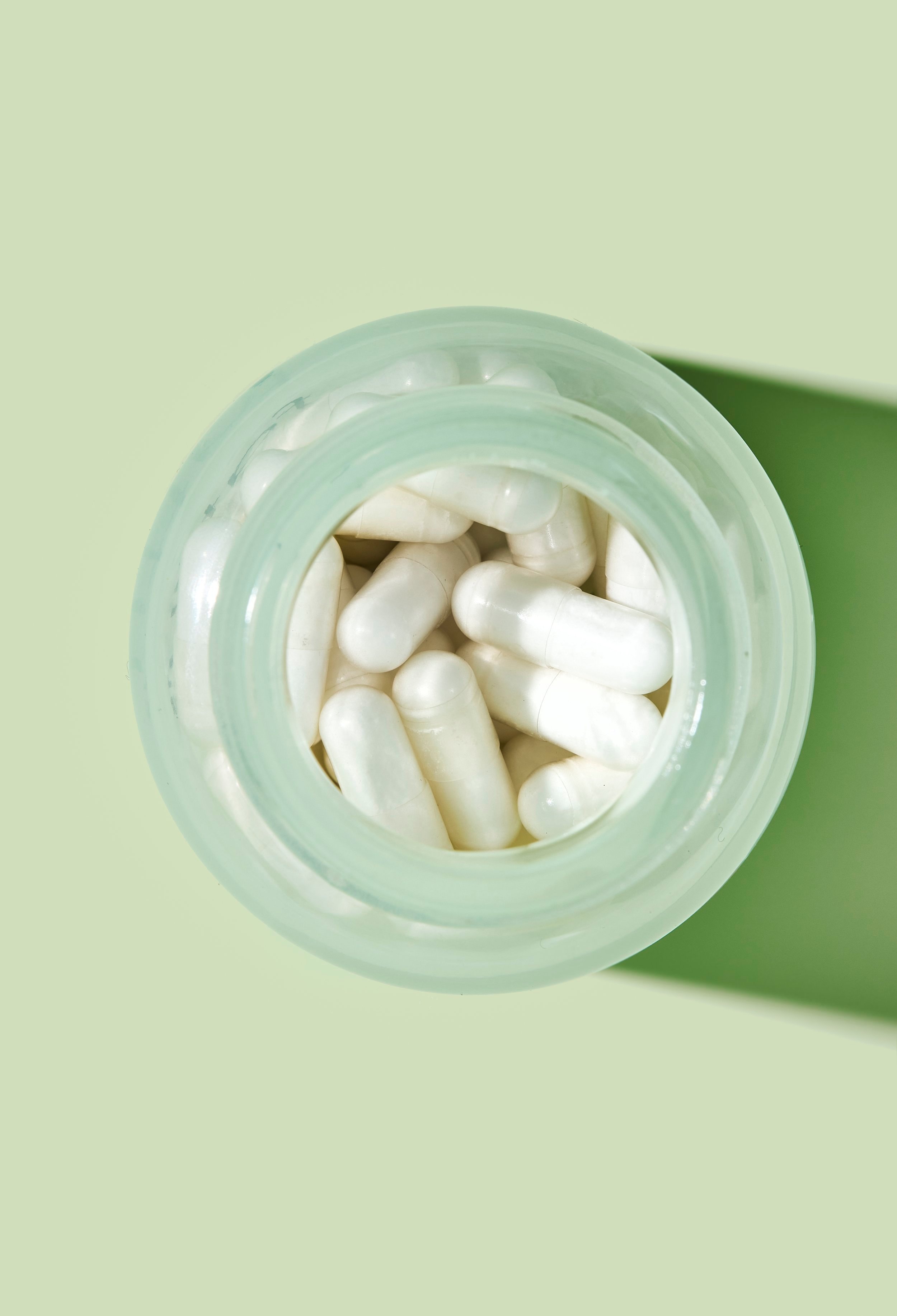 A glass bottle is viewed from above, full of many white fatty15 supplement pills.