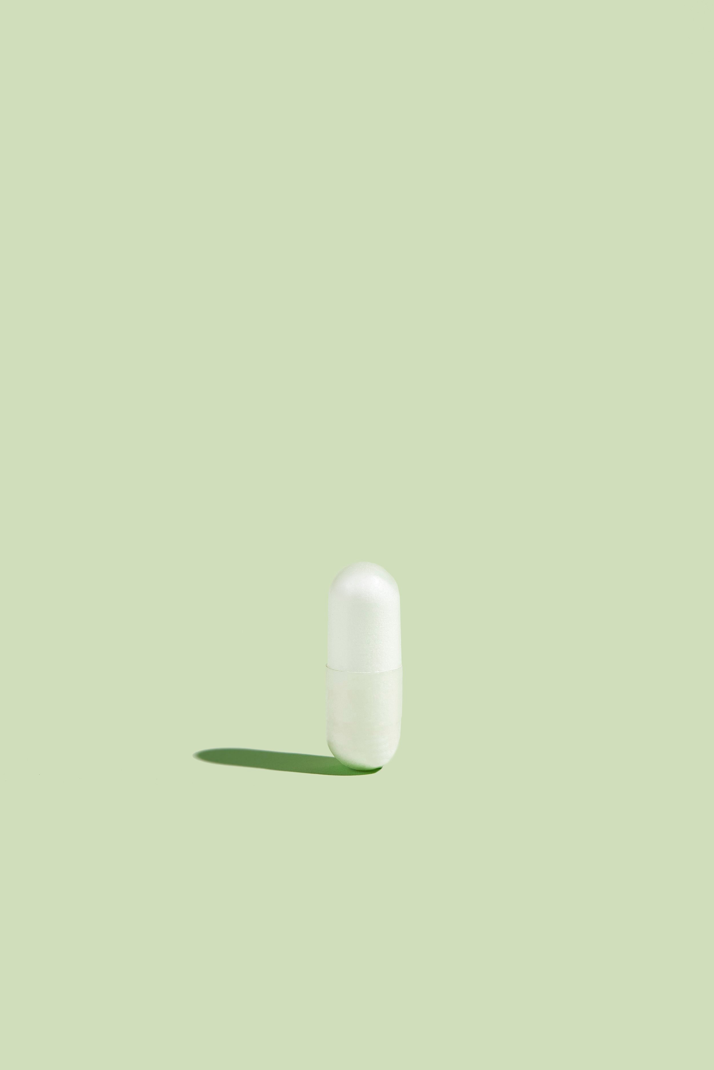 A single white fatty15 supplement pill sits on a green surface with a green background.