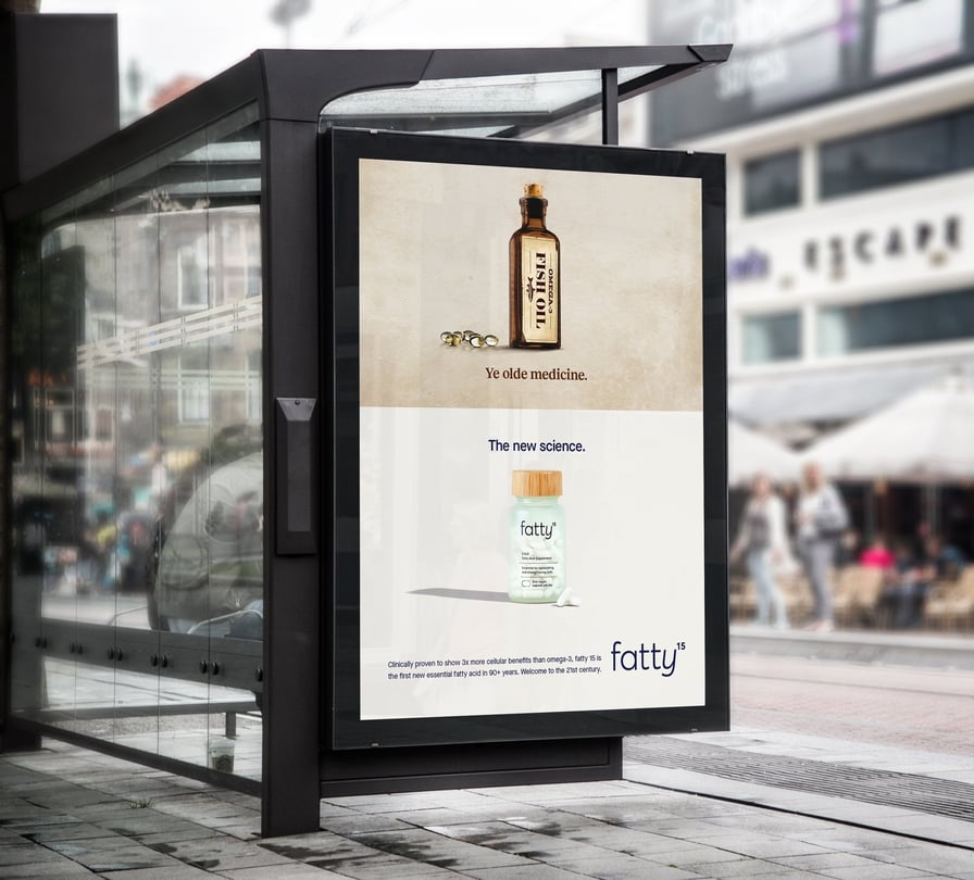 The image shows an ad in situation on the side of a bus stop shelter. The top, with an old fashioned fish oil bottle, reads "ye old medicine", while the bottom, with a clean new fatty15 supplement bottle, reads "the new science."