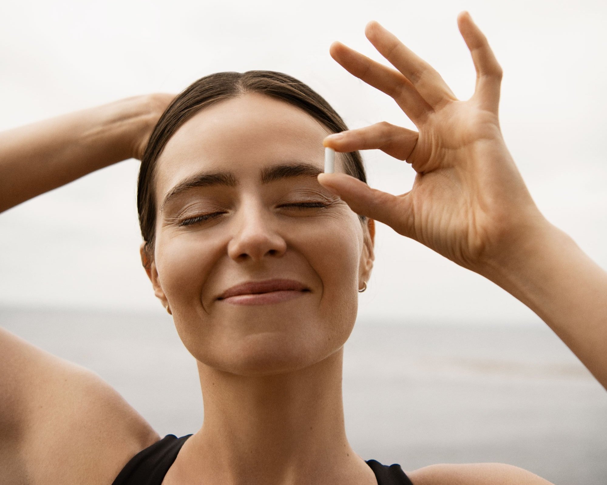 A woman in her early 30s looks happy and relaxed, holding up a single fatty15 supplement pill.