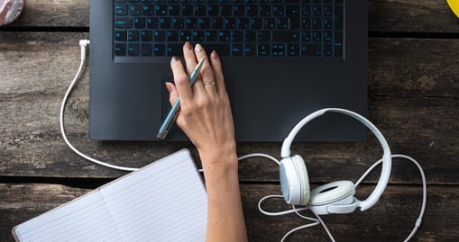 A person sitting at a desk, working on a laptop with earphones beside i