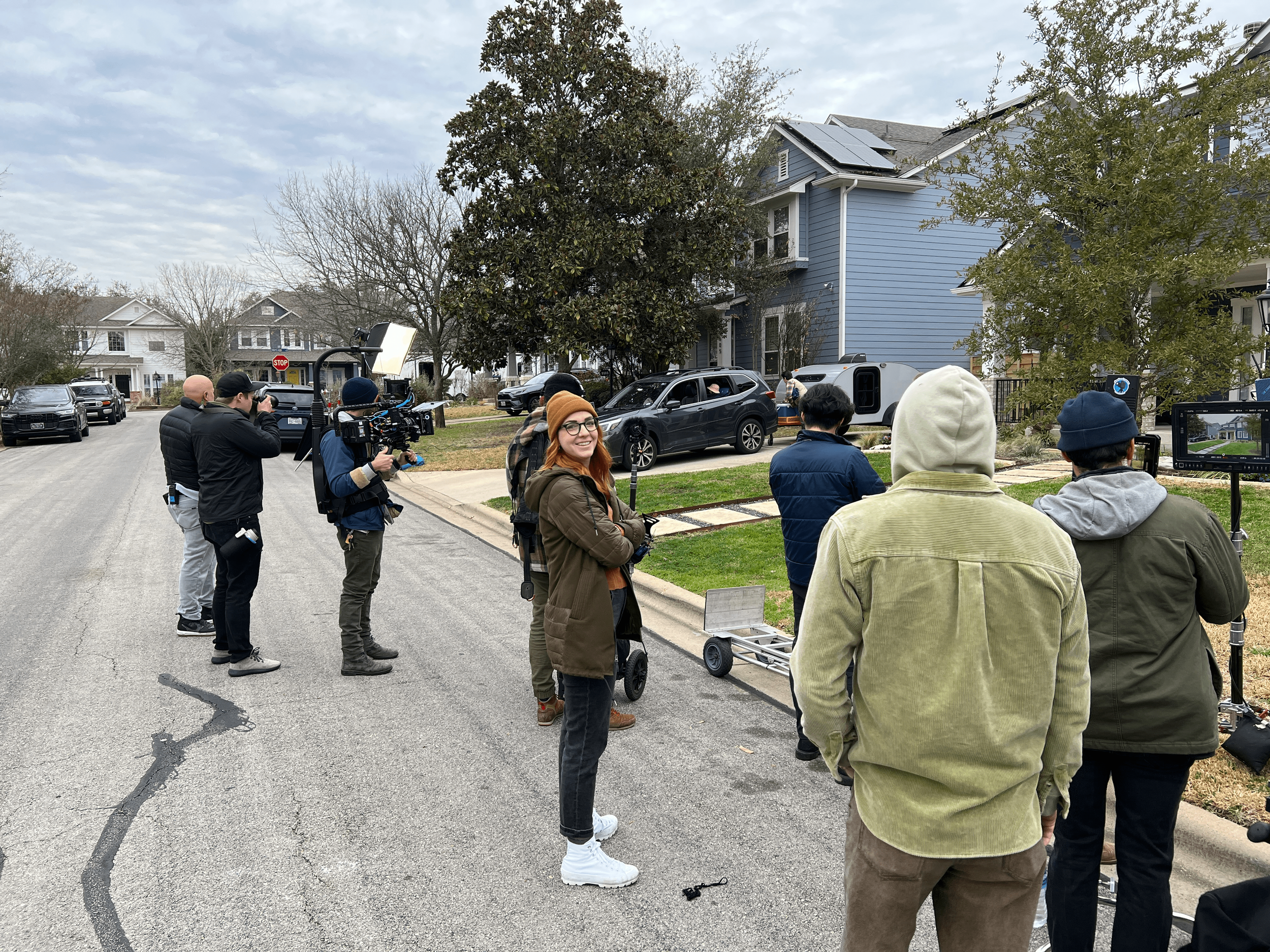 Devin Hilgenkamp, Door No. 3's Associate Creative Director, is wearing a dark green jacket, black jeans, white sneakers, and a burnt orange hat. She's standing amidst seven other members of a production crew during a film shoot.